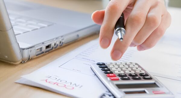 Person using a calculator and pen near a laptop on a desk.