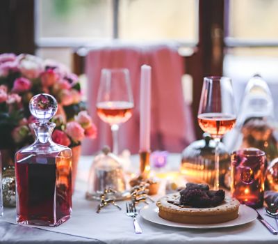 A cozy table setup with wine, cake, and flowers by the window.