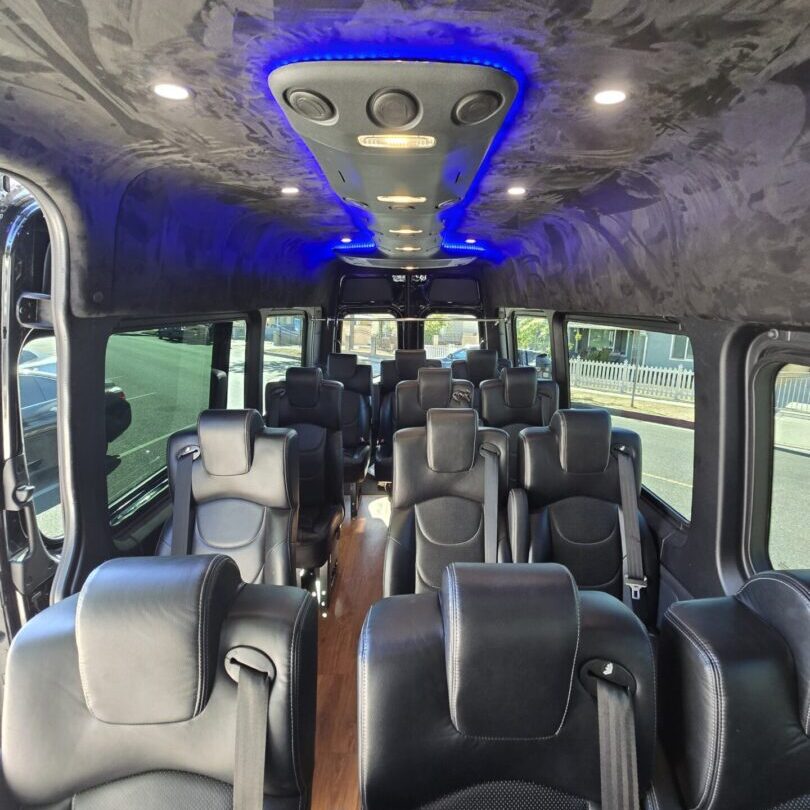 20241108_125951 Interior of a modern bus with blue LED ceiling lights and black leather seats.